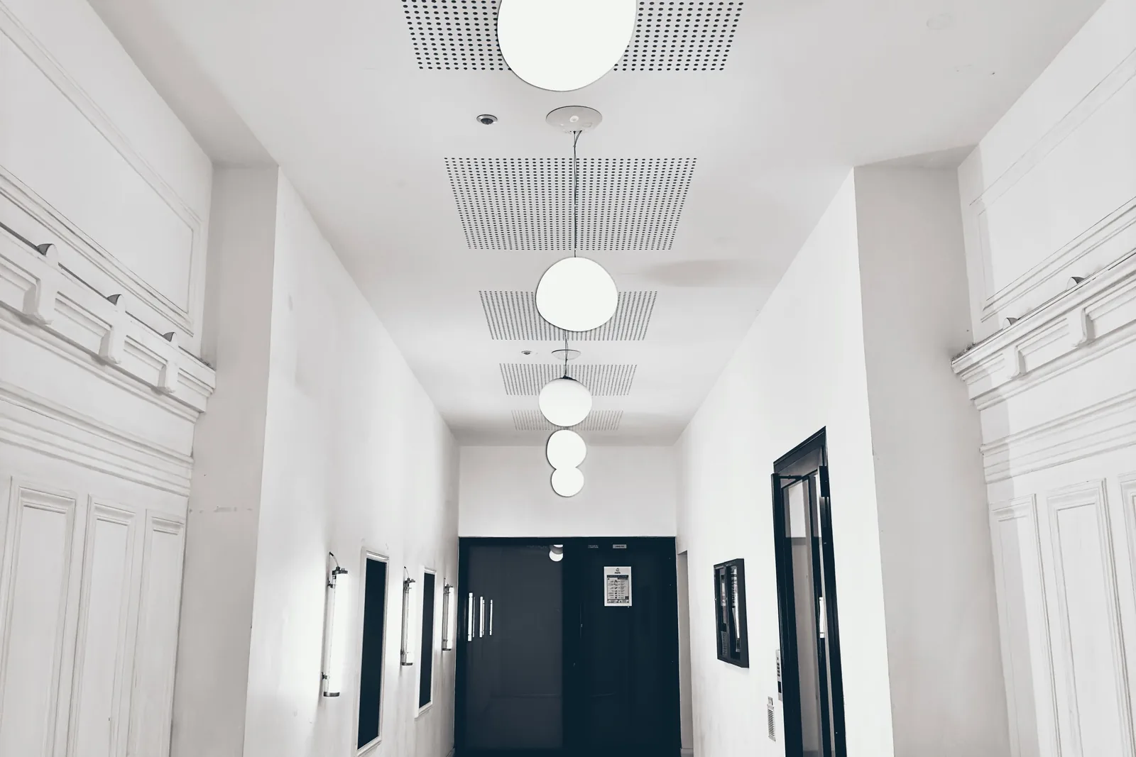Bright, minimalist white corridor with sculptural pendant lighting, representative of a modern clinical interior
