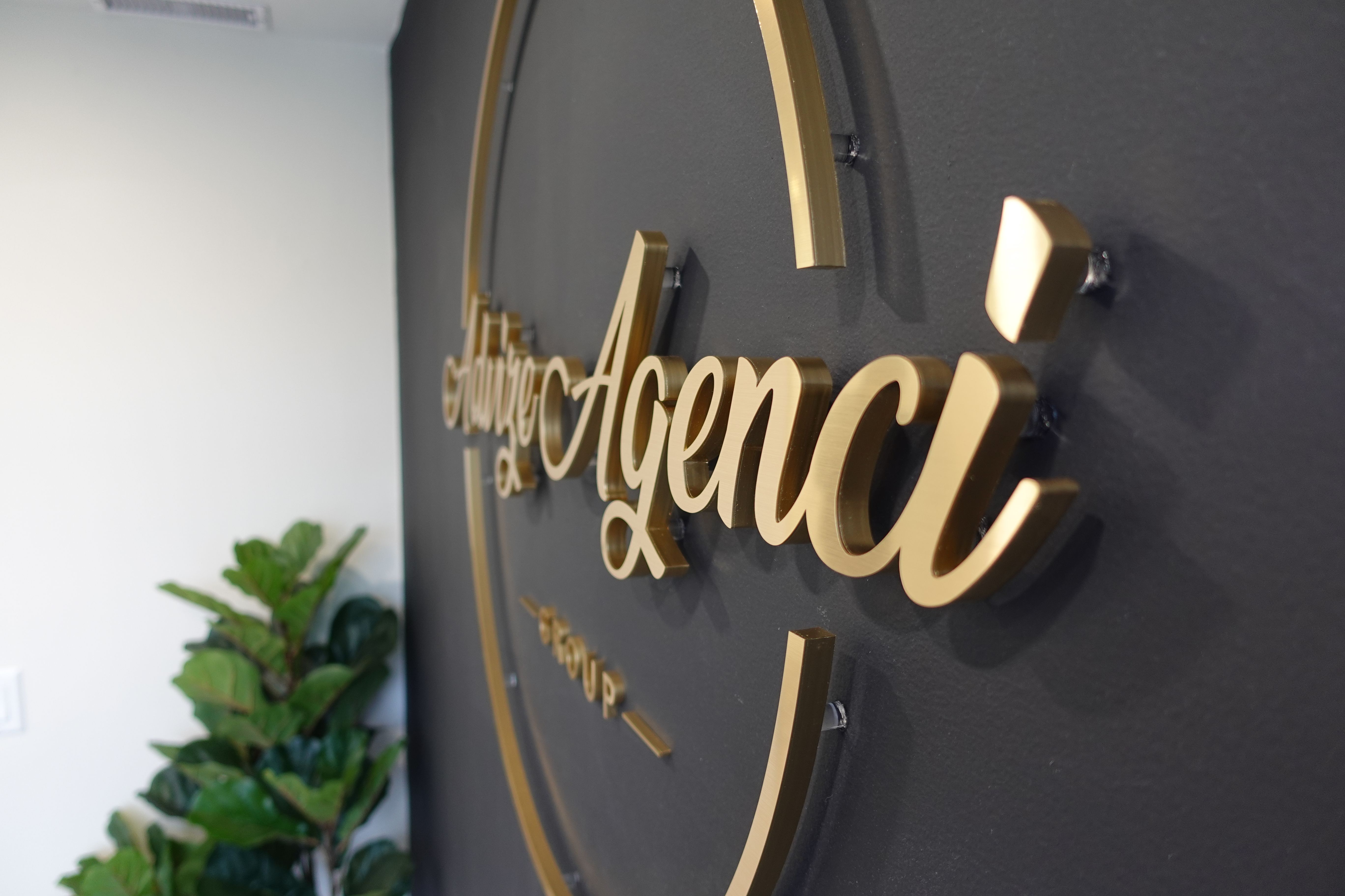 Brushed-gold dimensional reception logo sign installed in a premium dark-wall interior