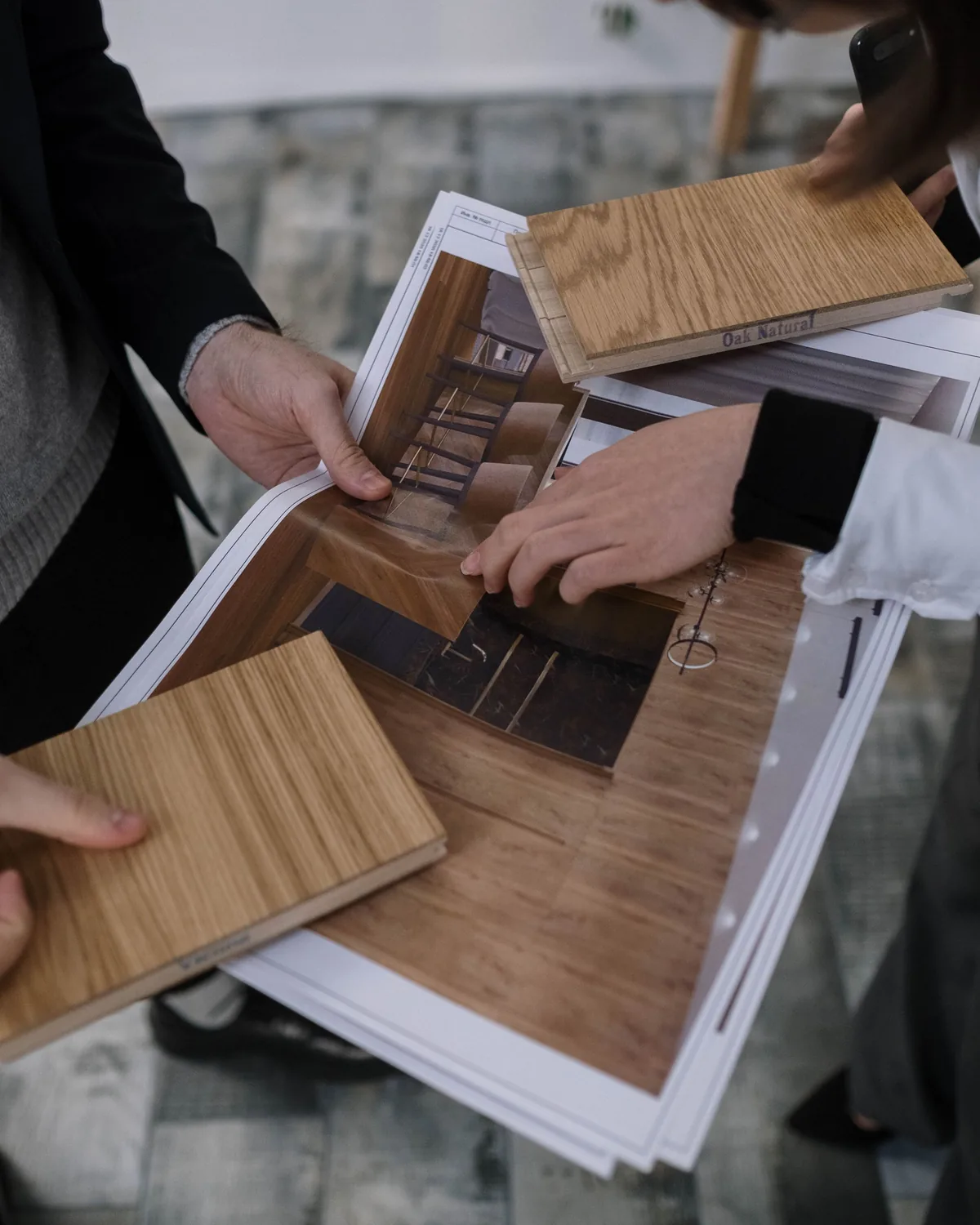 Hands reviewing wood material samples alongside interior specification drawings